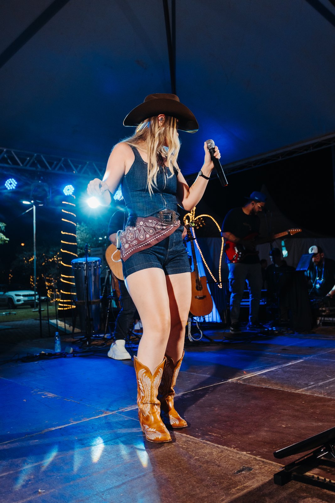 Mari Clemente cantando ao vivo no palco com microfone e botas country